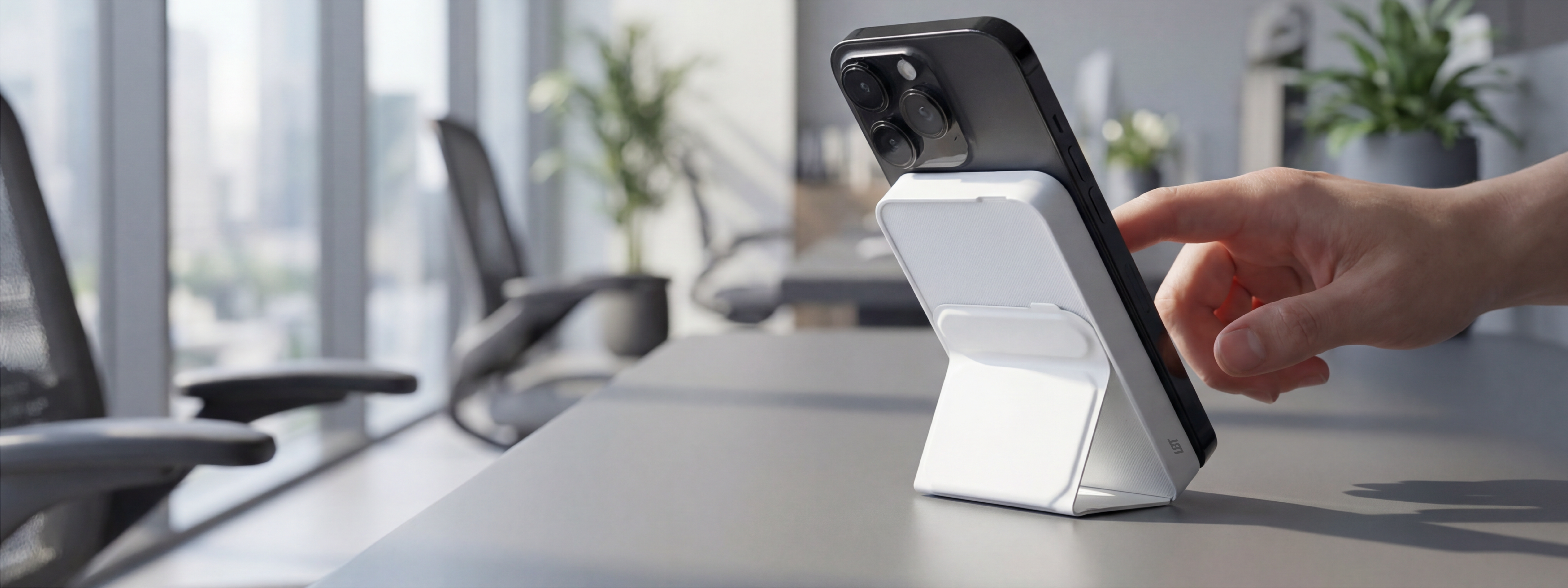 Hand using a smartphone with a charging stand on a desk in an office setting