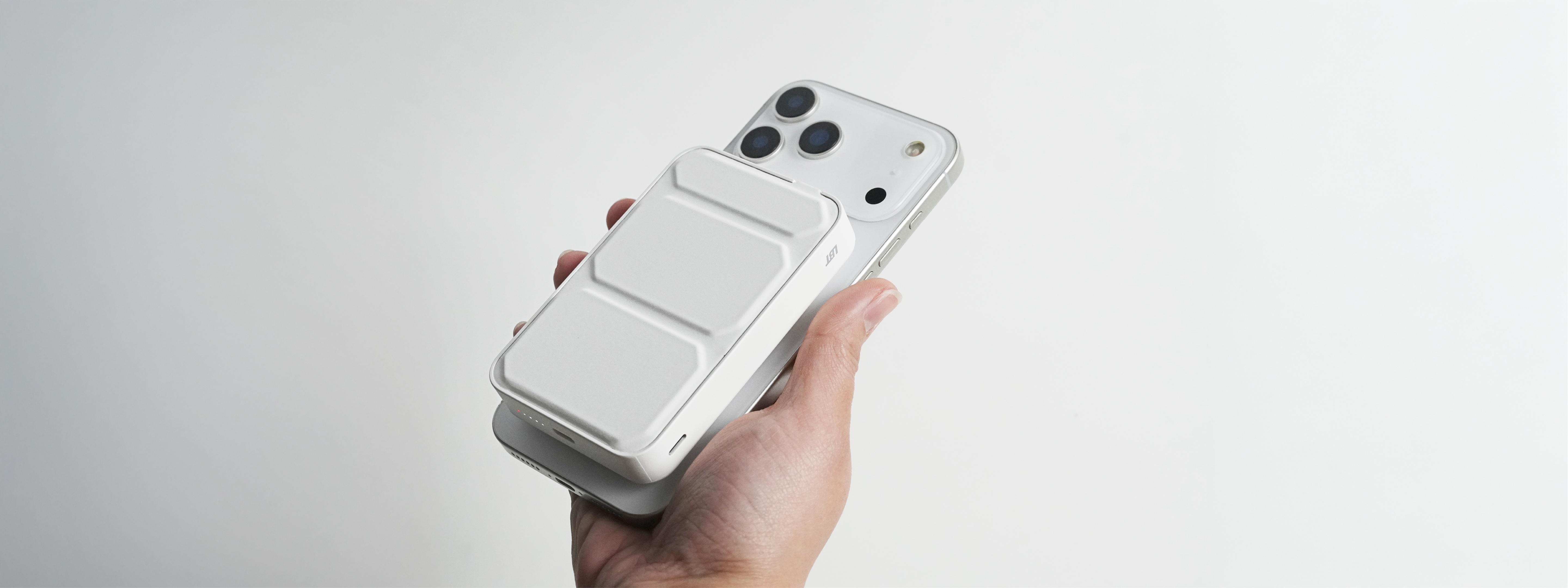 Hand holding a smartphone with a white power bank over the camera and screen on a light gray background